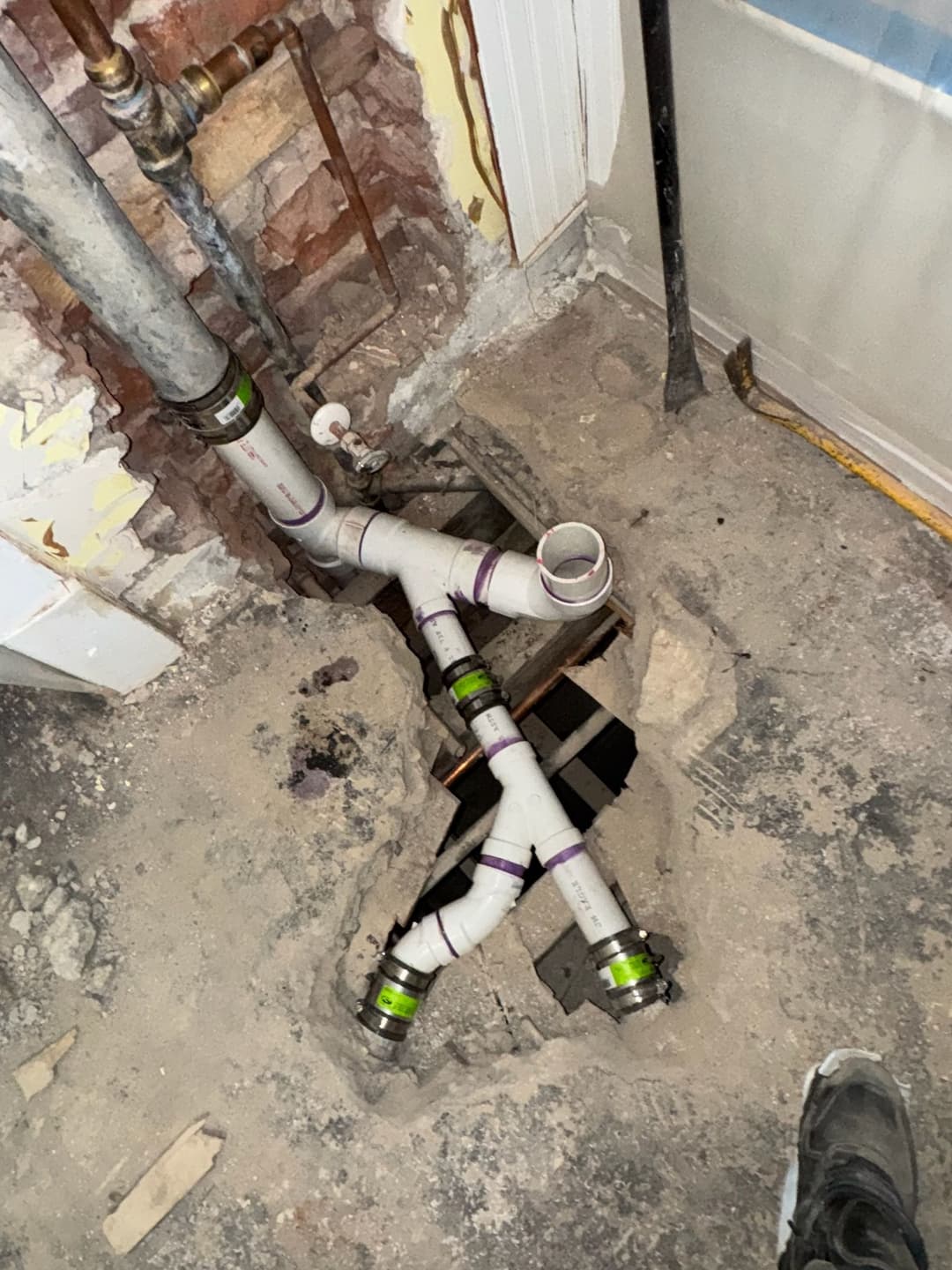 Exposed plumbing with PVC pipes and a floor opening in a construction site.