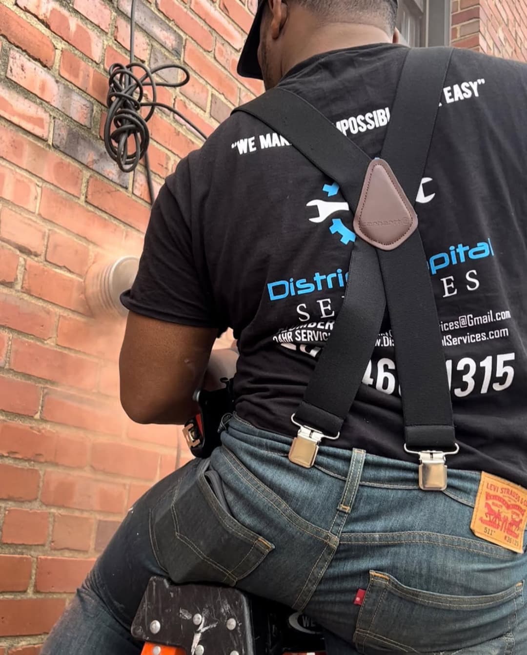 Worker using a power tool for masonry on a brick wall, safety gear visible.