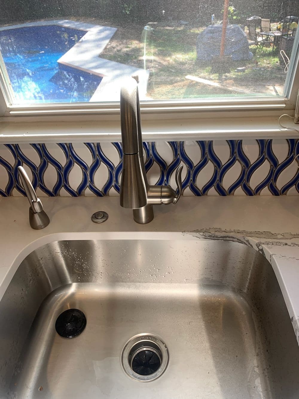 Modern kitchen sink with stainless steel faucet and decorative blue backsplash.