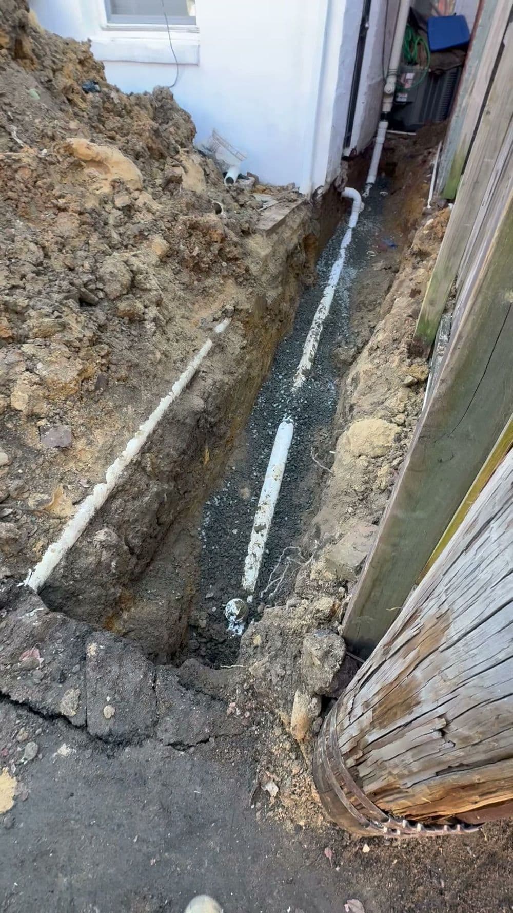 Excavated trench for plumbing installation with exposed white pipes and dirt pile.