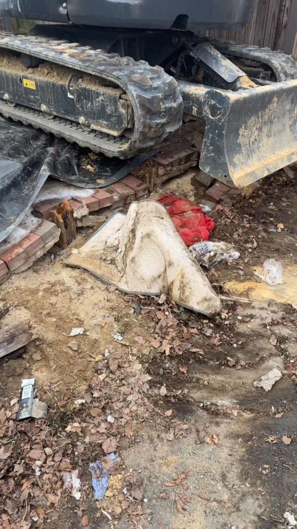 Excavator tracks on dirt with debris and a white object partially buried in leaves.