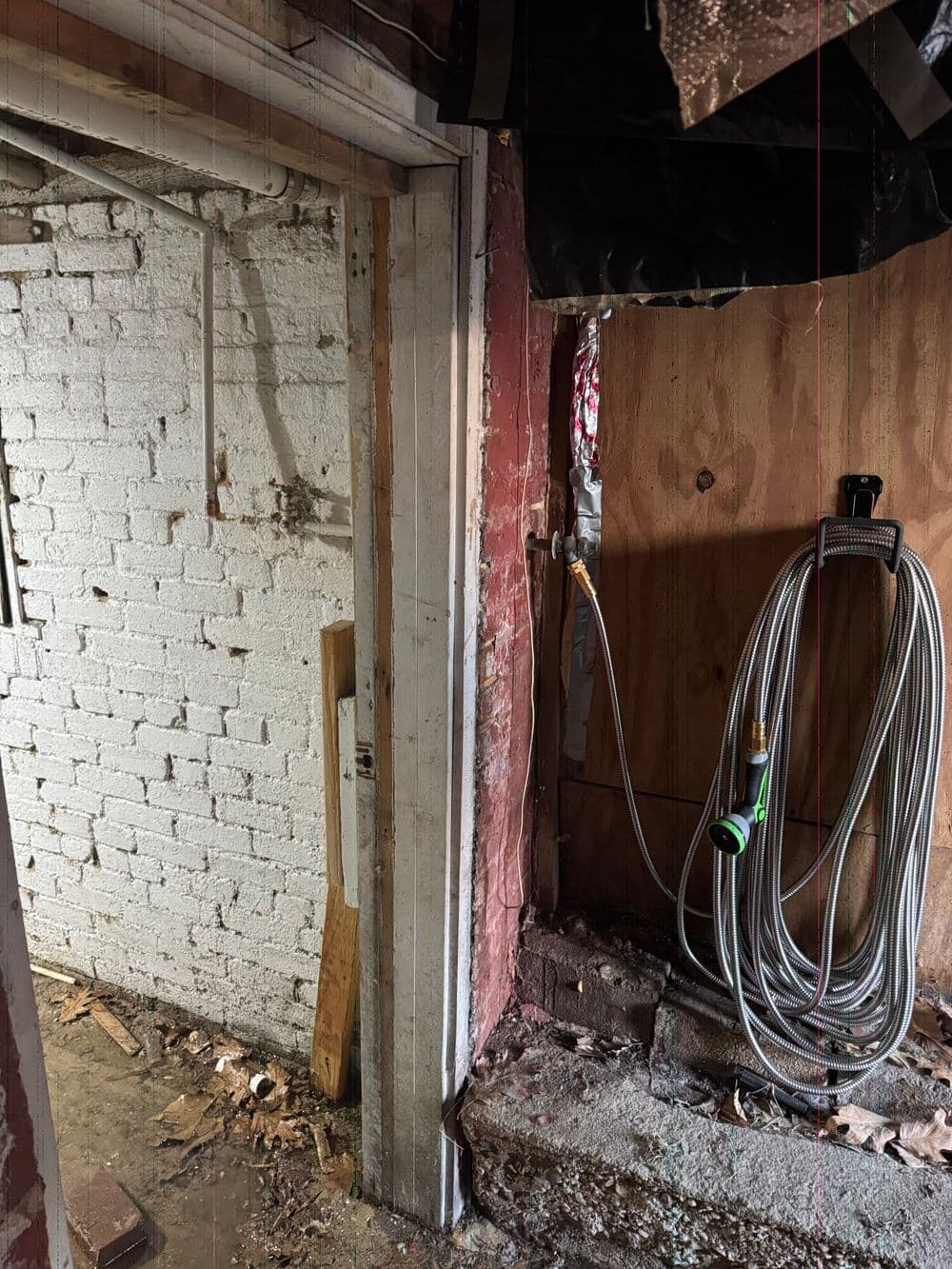 Interior view of an unfinished basement with exposed brick walls and a hose mounted on wood.