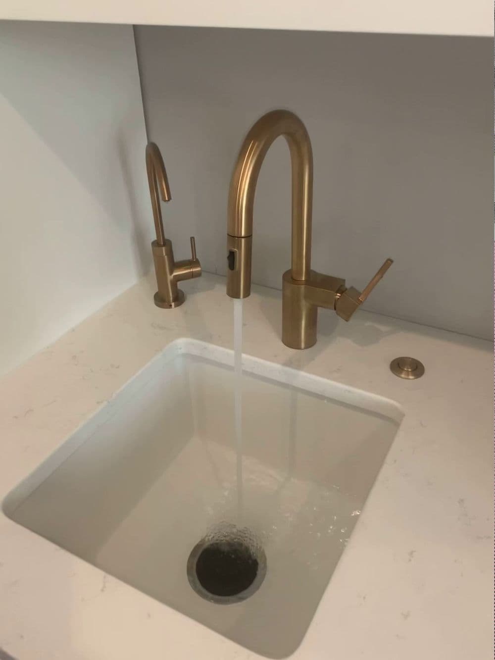 Modern bathroom sink with a stylish gold faucet and running water on a marble countertop.