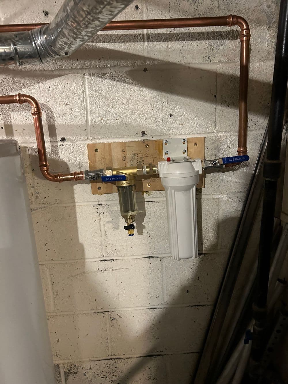 Water filtration system with copper pipes mounted on a wall in a basement.