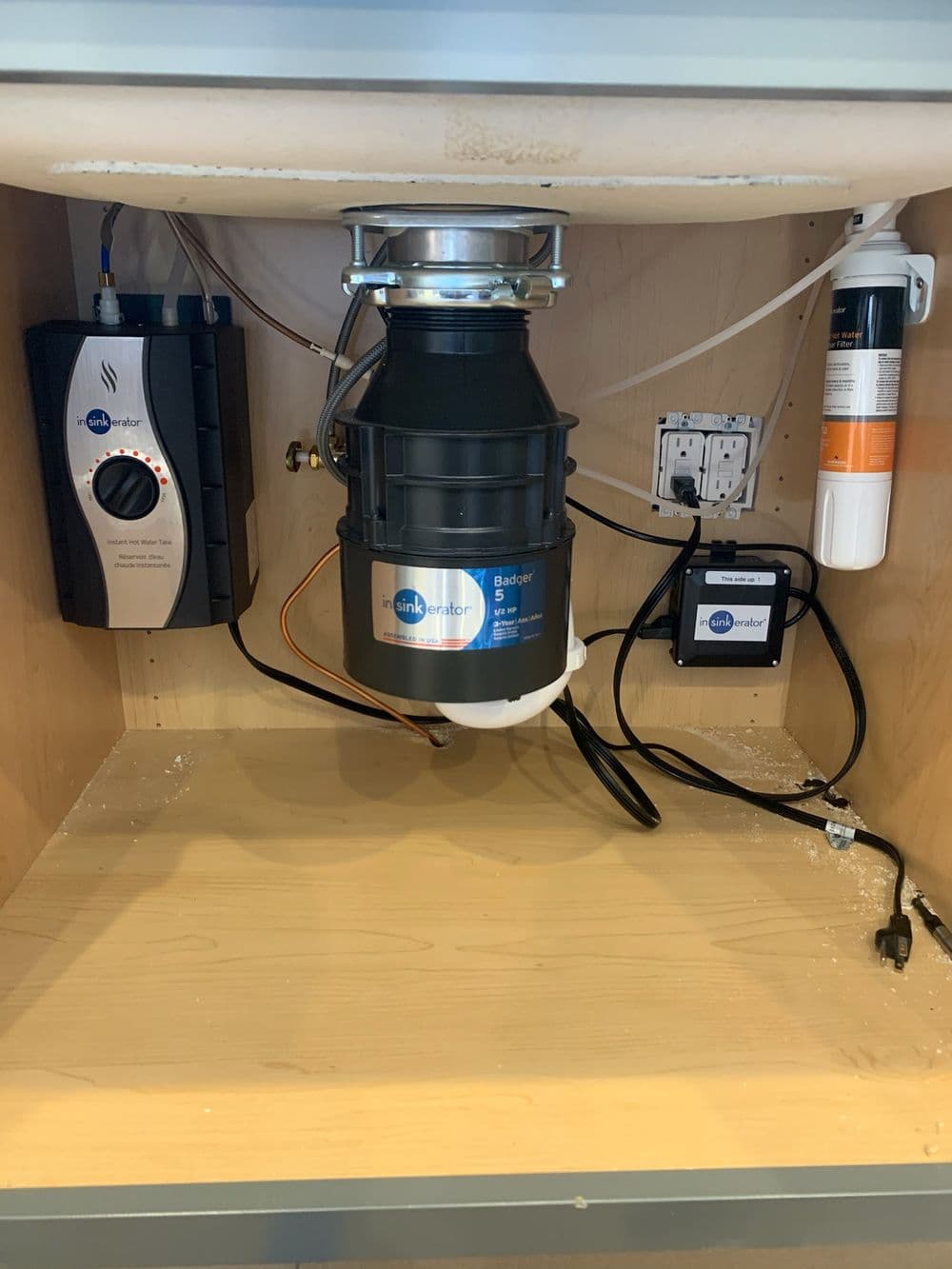 Insinkerator Badger 5 garbage disposal installation under kitchen sink with connected power system.