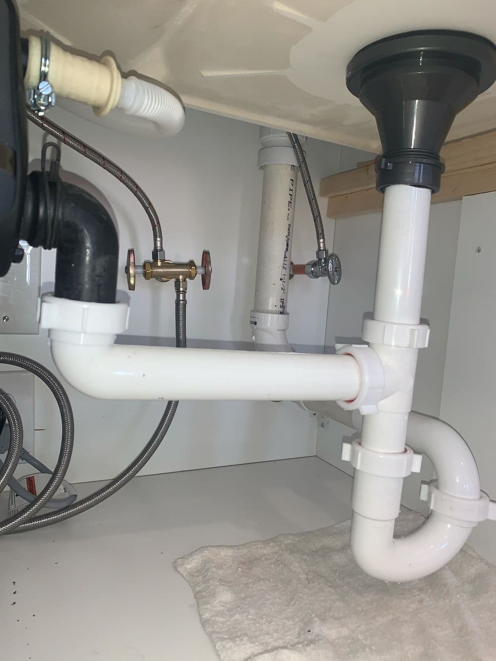 Under-sink plumbing setup with PVC pipes, shut-off valve, and drainage system.