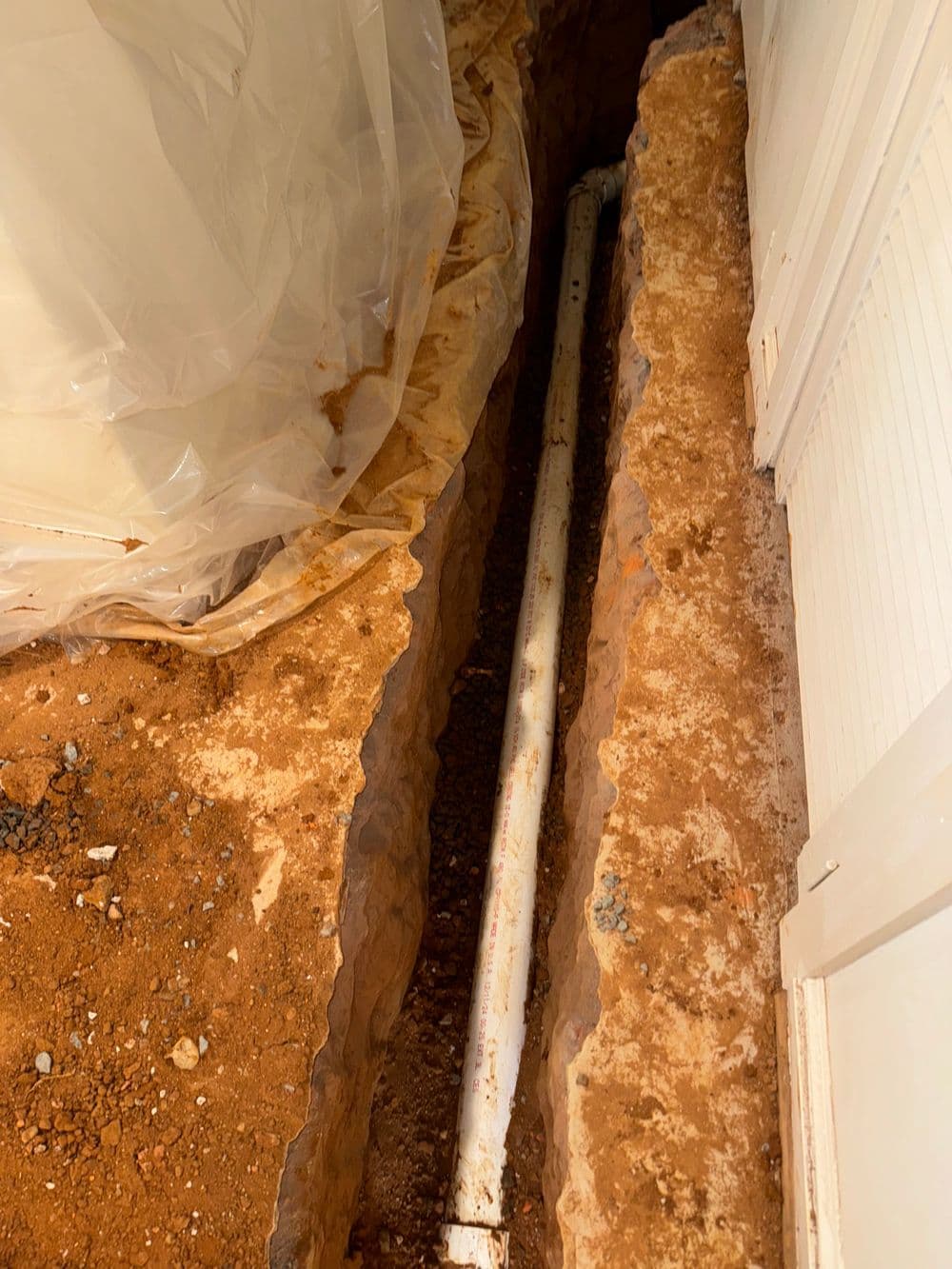 Excavated trench showing plumbing pipe installation in home renovation project.