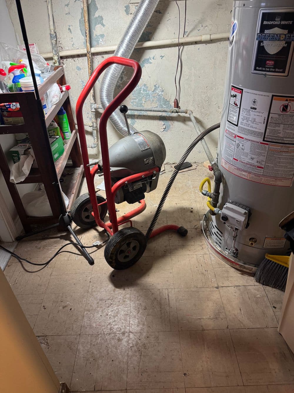Drain cleaning machine on a cart next to a water heater in a basement utility area.