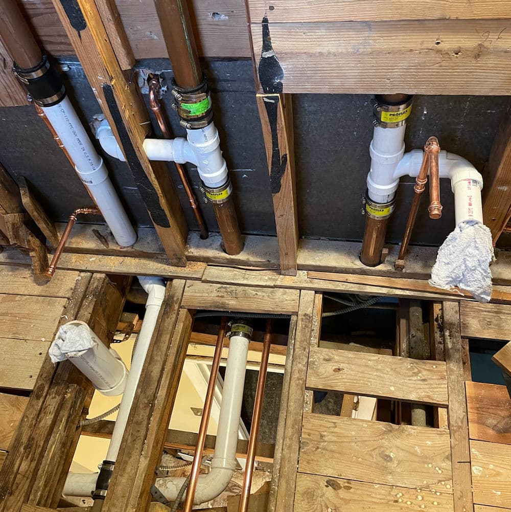 Exposed plumbing pipes and wooden beams in a remodelled home renovation project.