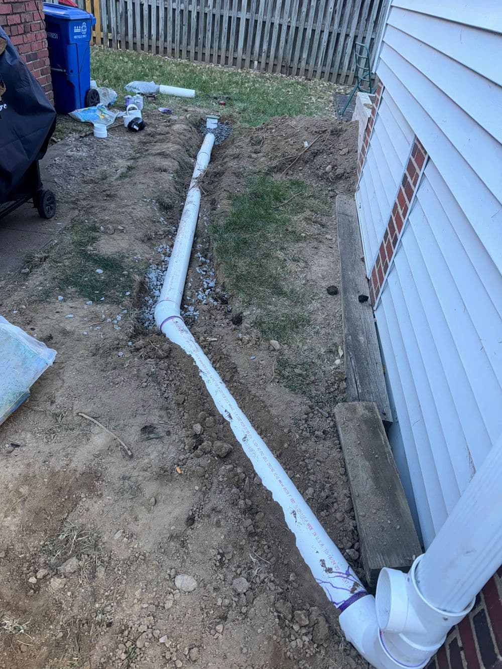 Residential yard with buried white drainage pipes and an excavated trench beside a house.