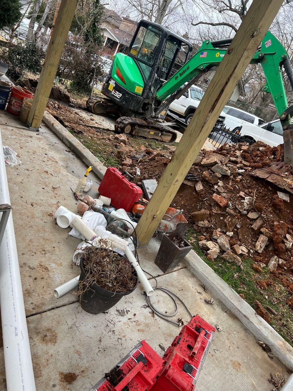 Excavator and construction debris near home with scattered tools and materials.