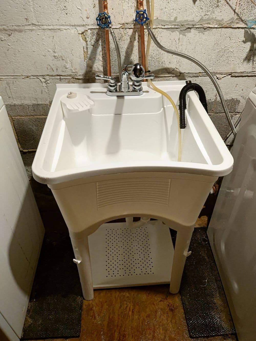 White utility sink with faucet and connected water hoses in a basement laundry area.