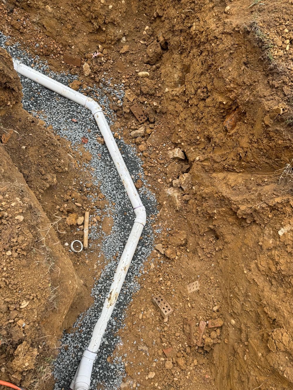 Excavated trench with white piping and gravel for drainage installation.