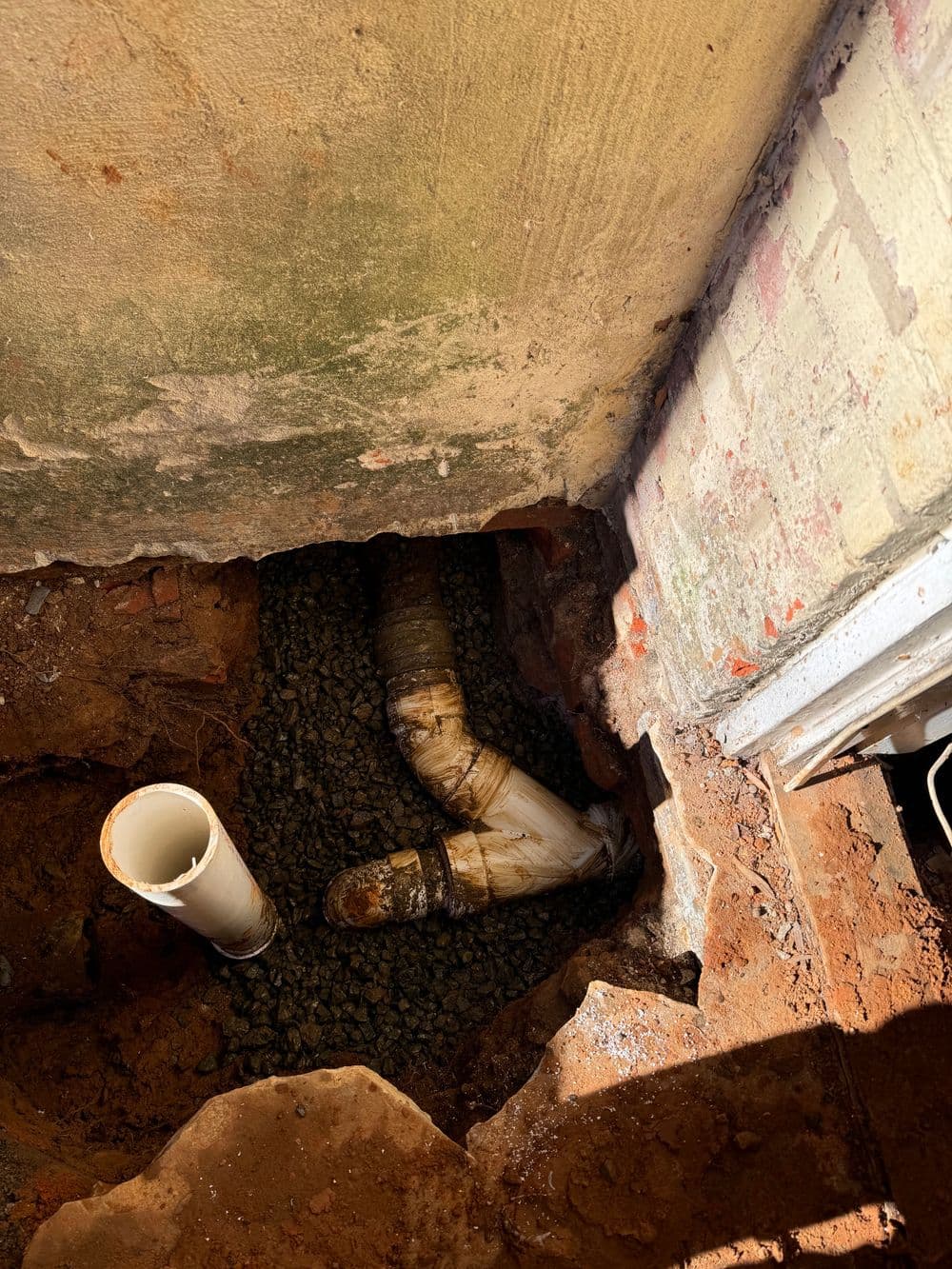 exposed drainage pipe in a dug trench near a building's foundation with gravel bedding