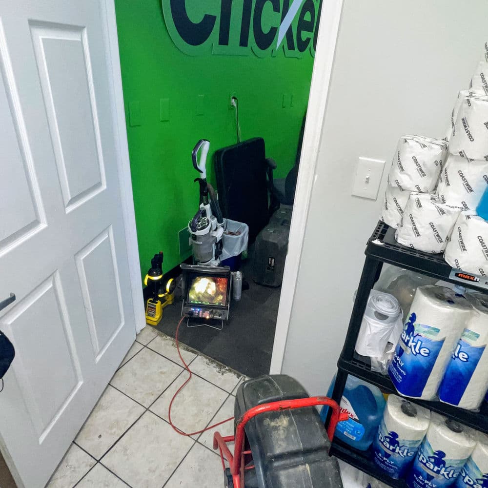 Cluttered room with green wall, cleaning equipment, and storage shelves visible.