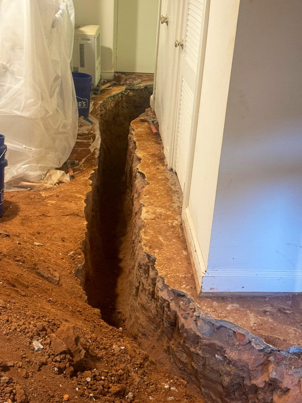 Excavated trench in home renovation, exposing foundation with construction materials nearby.