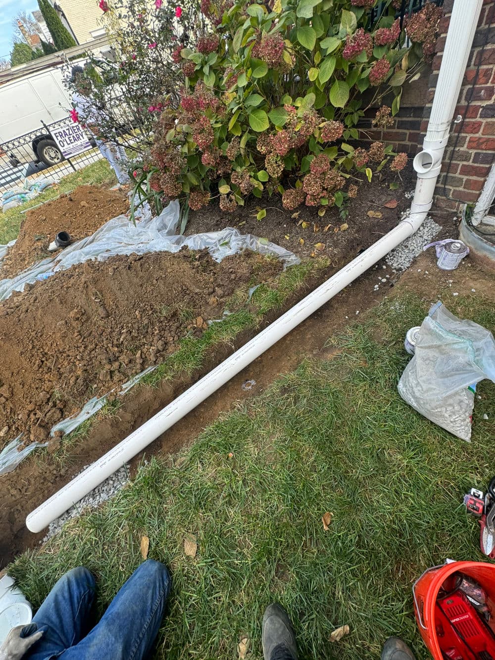 Installation of a white drainage pipe in a garden with soil and plants nearby.