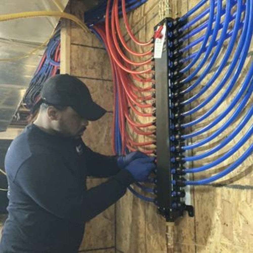 Technician installing plumbing system with blue and red pipes on a wall panel.
